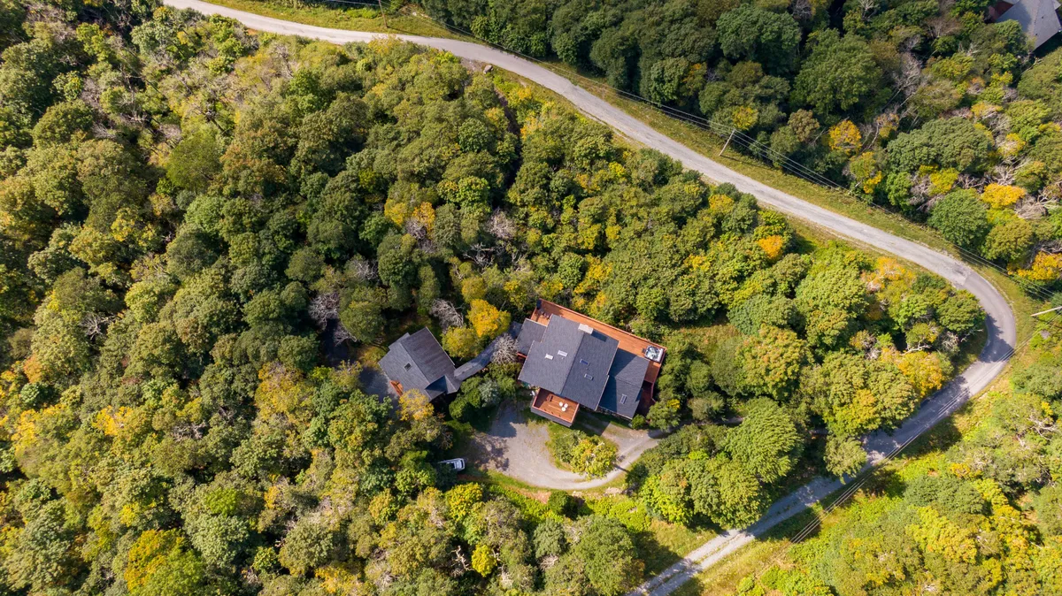 A tranquil view of the main house set against a backdrop of lush trees and a gently winding road. The scene suggests easy access to nearby trails and opportunities for bird watching, outdoor meals, or unwinding after a day of adventure.