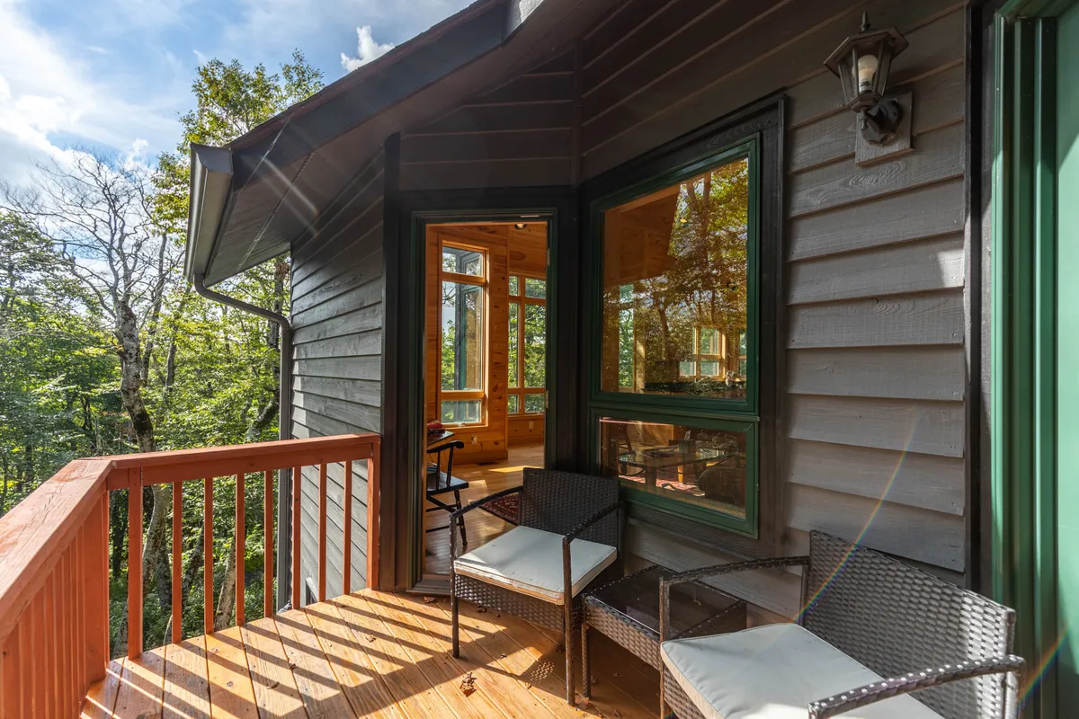 A tranquil wooden deck and balcony extend from the chalet, surrounded by towering trees and illuminated by soft natural light. Large windows hint at cozy spaces inside, while the deck invites couples to relax with a book, enjoy morning coffee, or watch the sunset together.