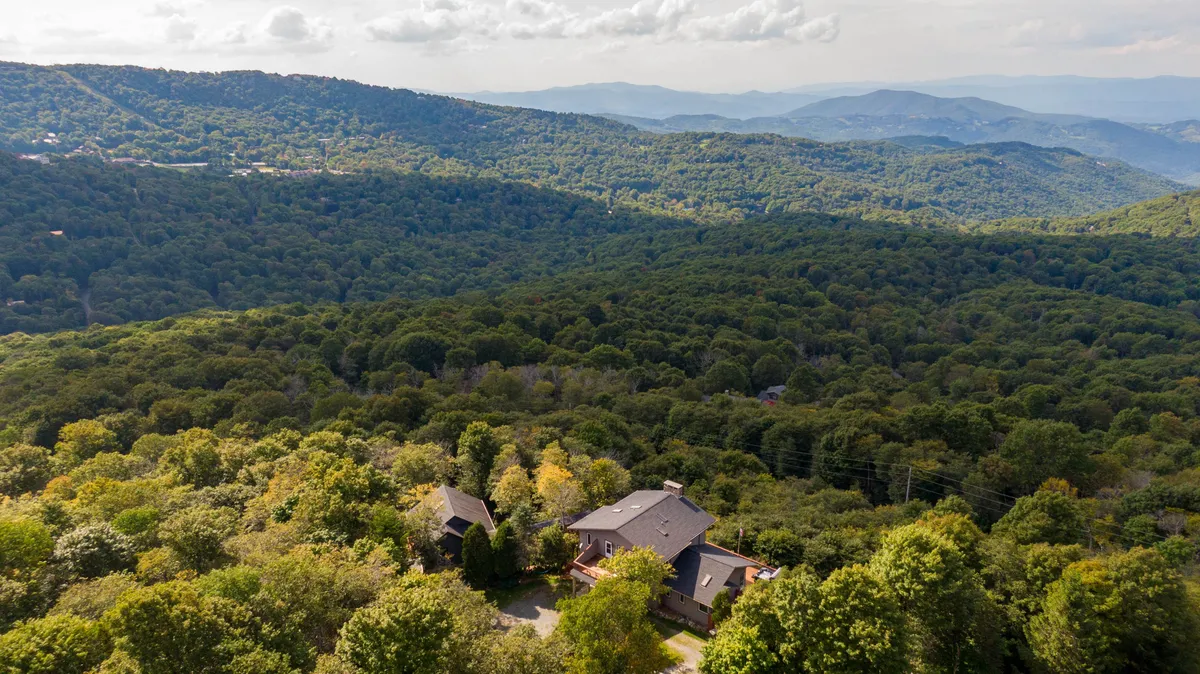 A breathtaking, wide-angle view of the Blue Ridge Mountains stretches into the distance, framed by lush trees and the chalet property nestled in the foreground. The deck, perched high above the valley, offers an unobstructed vantage point for taking in vibrant sunsets, starry nights, and the rolling landscape below.