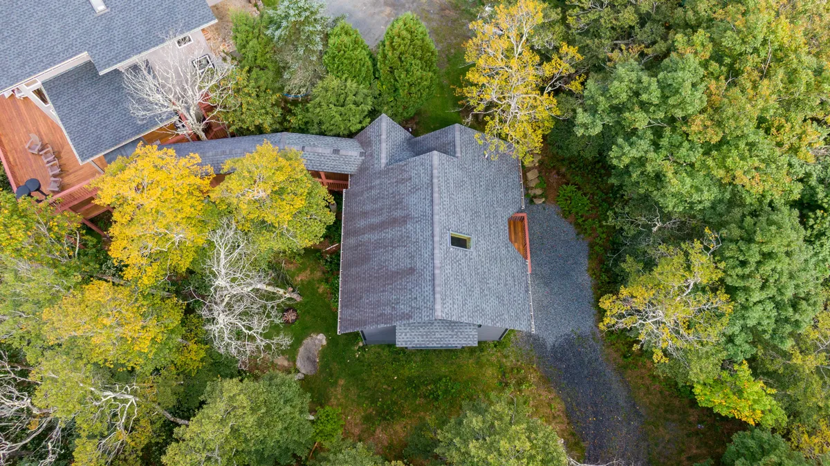 This exterior shot captures the chalet nestled among towering trees, with a clear view of the house, the meandering pathway, and inviting outdoor spaces. The natural landscape hints at year-round possibilities for nature walks and outdoor gatherings, perfectly illustrating the home's proximity to adventure.