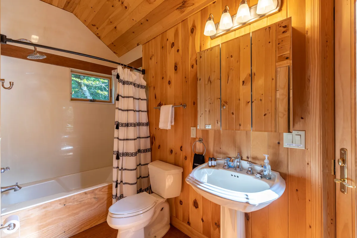 A bright, inviting bathroom with a wooden interior, modern sink area, and a shower curtain. The space is awash in natural light, creating a refreshing, spa-like ambiance perfect for morning routines or a relaxing evening bath.