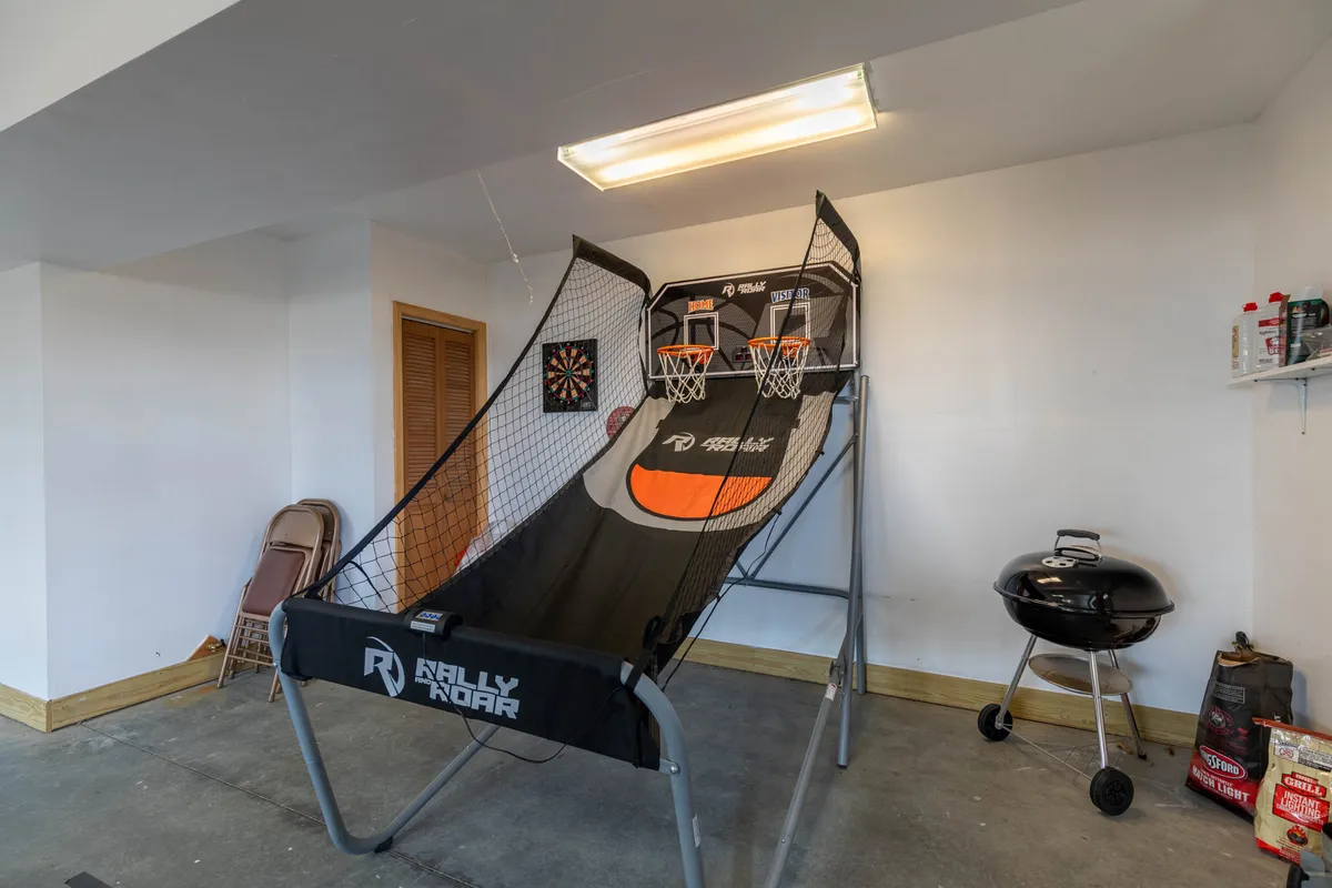 A glimpse inside a vibrant game room featuring a basketball arcade game, dartboard, and a grill setup. The space is designed for fun and socializing, providing indoor entertainment after a day spent outdoors. The relaxed mood hints at comfortable moments spent with family, friends, and pets.